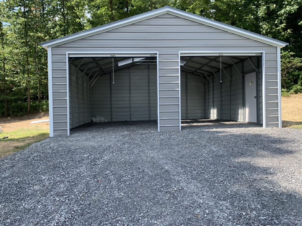 A light grey roofed and walled carport with white trim, built on a gravel driveway.