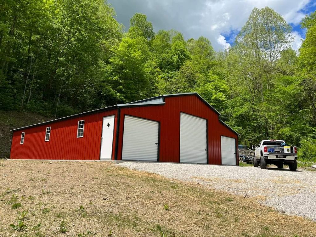 A large metal barn with red siding and white trim built on a small hill