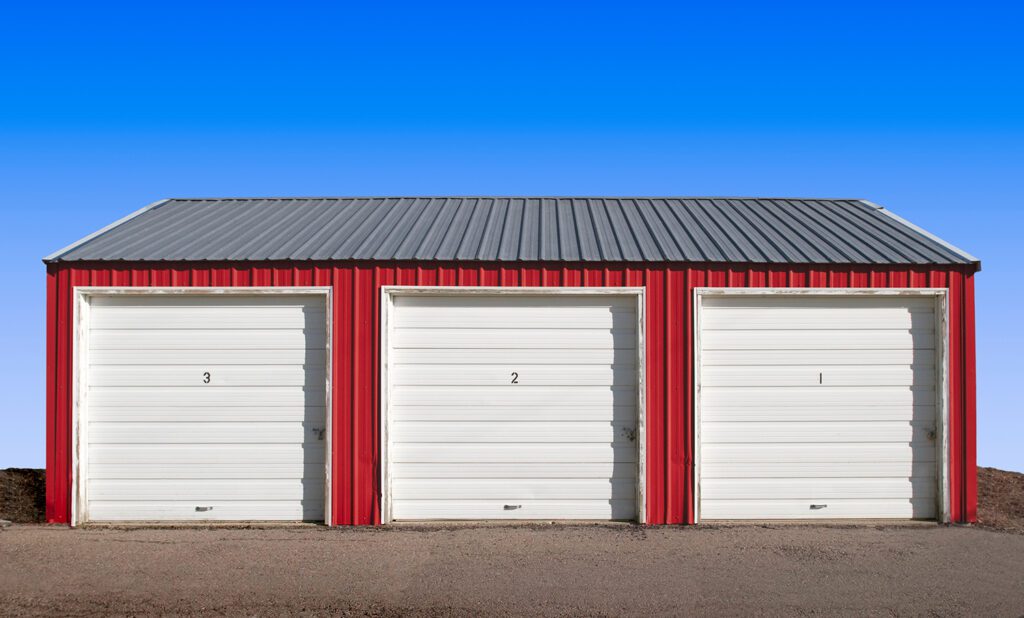 A red garage port and storage shed with 3 separate doors.